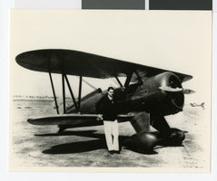 Photograph of Howard Hughes standing beside his modified biplane, circa 1934