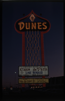 Color view of the Dunes Hotel marquee at dusk. The Casin de Paris, Line Renaud, and Vive Les Girls! are featured.