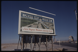 Color view of a billboard advertising the projected opening in March 1966 "Las Vegas' Newest Luxury hotel!" The Flamingo marquee featuring Jack Carter is visible in the background.