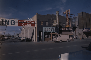 Color view of Fremont Street. A parking sign for the Nevada Club, the Saratoga Race Book, Famous Pioneer and Mike's Liquors are visible.