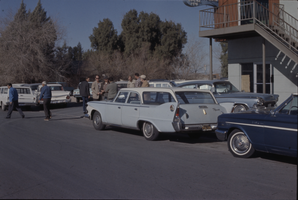 Color view of several men talking in a parking lot.