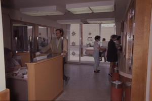 Color view of several people waiting to be helped in an open office and service desk area.