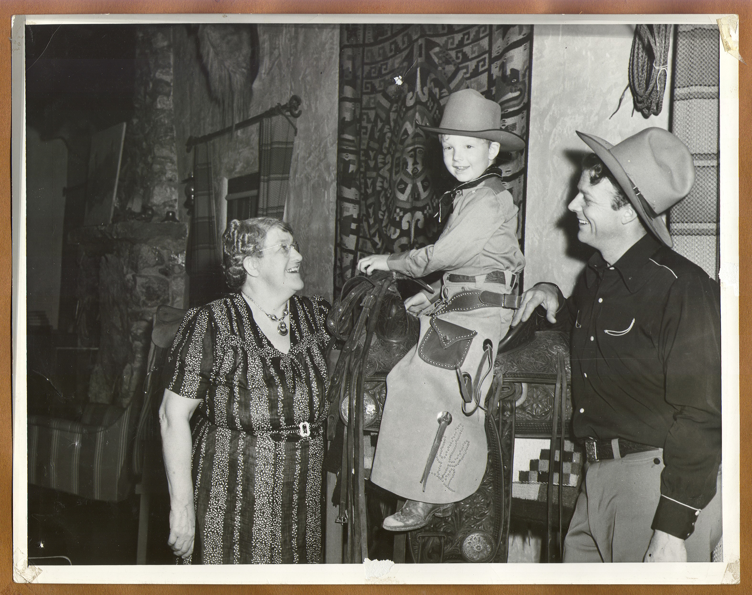 Rex Bell and Grandma Beldam with Rex Bell Jr. who is dressed in cowboy gear, seated on a saddle: photographic print