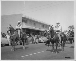 Rex Bell (George Francis Beldam) and M.C. Earl on horseback in a parade in Palm Springs in 1952. Handwritten on back: Rex Bell, MC Earl, Palm Spgs, 1952