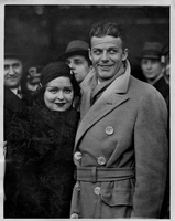 Rex Bell (George Francis Beldam) and Clara Bow while on their trip to Europe with a group of unidentified people at Waterloo Station, London. Labeled on back: Miss Clara Bow, the film acress famed as the "It" girl, accompanied by her rancher husband, Mr. Rex Bell who is also a film actor, arrives at Waterloo Station, London, from America.  Miss Clara Bow,with her rancher husband Mr. Rex Bell on the platform at Waterloo Station, W., S. & G., 21/12/32. Stamped on back: This photograph must not be reproduced i