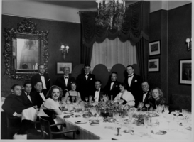 Clara Bow (Left side of table) and Rex Bell (George Francis Beldam)(center) with a group at a dinner party. Handwritten on back:"Berlin January 1, 1933" and many illegible names.  Also includes a stamp in German