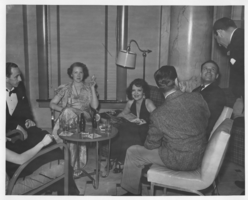 Clara Bow (seated under lamp) and Rex Bell (George Francis Beldam)(seated to the right of her) with five unidentified people in 1939