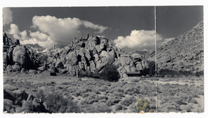 Photograph of cabins below rock outcropping, early 1900s