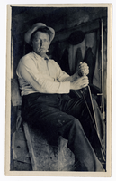 Photograph of a seated man holding machine levers, Goldfield (Nev.), early 1900s