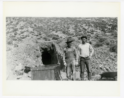 Photograph of two men with an ore cart standing at a mine adit, 1900-1925