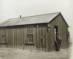 Photograph of railroad surveyor next to building, circa 1890s-1910