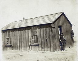 Photograph of man beside wooden building, circa 1900-1920s