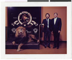 Photograph of two unidentified men posing with the MGM Grand Hotel, Reno publicity display and lion, location unknown, circa 1990s