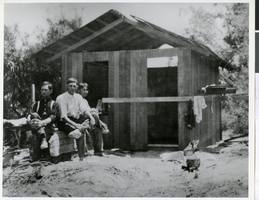 Photograph of three men sitting in front of a cabin, possibly Nevada, circa 1900s