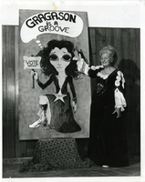 Photograph of Bonnie Gragson, wife of Mayor Oran K. Gragson, in a Renaissance-style costume displaying a campaign poster for her husband, circa 1960s