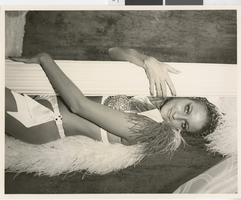 Photograph of a showgirl in a feathered costume, hugging a stage column, Dunes Hotel, Las Vegas (Nev.), 1957-1960s