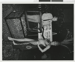 Photograph of a Minsky showgirl posing in front of a poster at the Aladdin Hotel, Las Vegas (Nev.), 1972
