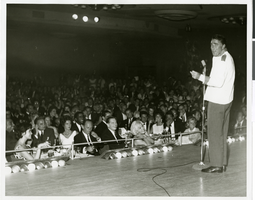 Photograph of Peter Lawford performing at the Copa Room in the Sands Hotel with several celebrities in the audience, Las Vegas, circa 1960