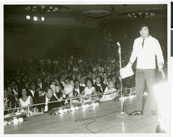 Photograph of Peter Lawford onstage at the Copa Room in the Sands Hotel with several celebrities in the audience, Las Vegas, circa 1960