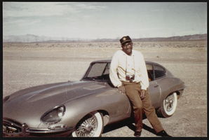 James B. McMillan posing by his sports car with a camera: photographic print