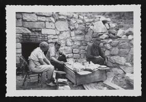 Hazel Denton, her son Lewis, and her husband Floyd seated around large wooden box topped with food in ruins of a stone house in Hiko, Nevada: photographic print
