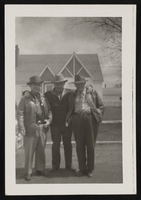 Three men posed in the road in front of a house: photographic print