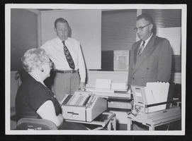 People in an office looking at a typewriter: photographic print