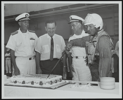 Rear Admiral F. J. Brush and Captain W. E. Clarke watch as Lieutenant Commander C. D. Wheeler cuts a cake: photographic print