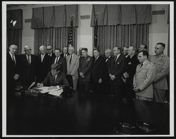 Howard Cannon, congressmen, and military leaders observe President John F. Kennedy signing official documents: photographic print