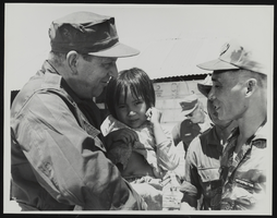 Howard Cannon holding a Vietnamese child while standing with an interpreter: photographic print