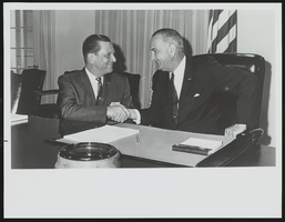 Howard Cannon, seated at desk, shaking hands with Lyndon B. Johnson: photographic print