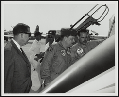 Howard Cannon on an airfield next to an aircraft speaking to two unidentified men: photographic print
