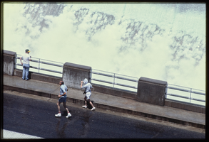 People make their way through the water spray caused by overflow water in the Arizona spillway, looking west at Hoover Dam, Arizona: photographic slide