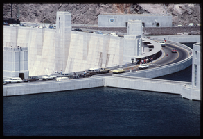 Water reaches the high point as automobiles and pedestrians cross the top of the dam as seen from above the Arizona spillway, looking southwest towards the Nevada side at Hoover Dam, Arizona: photographic slide