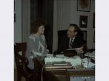 Film negative of Chic Hecht seated at a desk speaking with woman, February 26, 1988