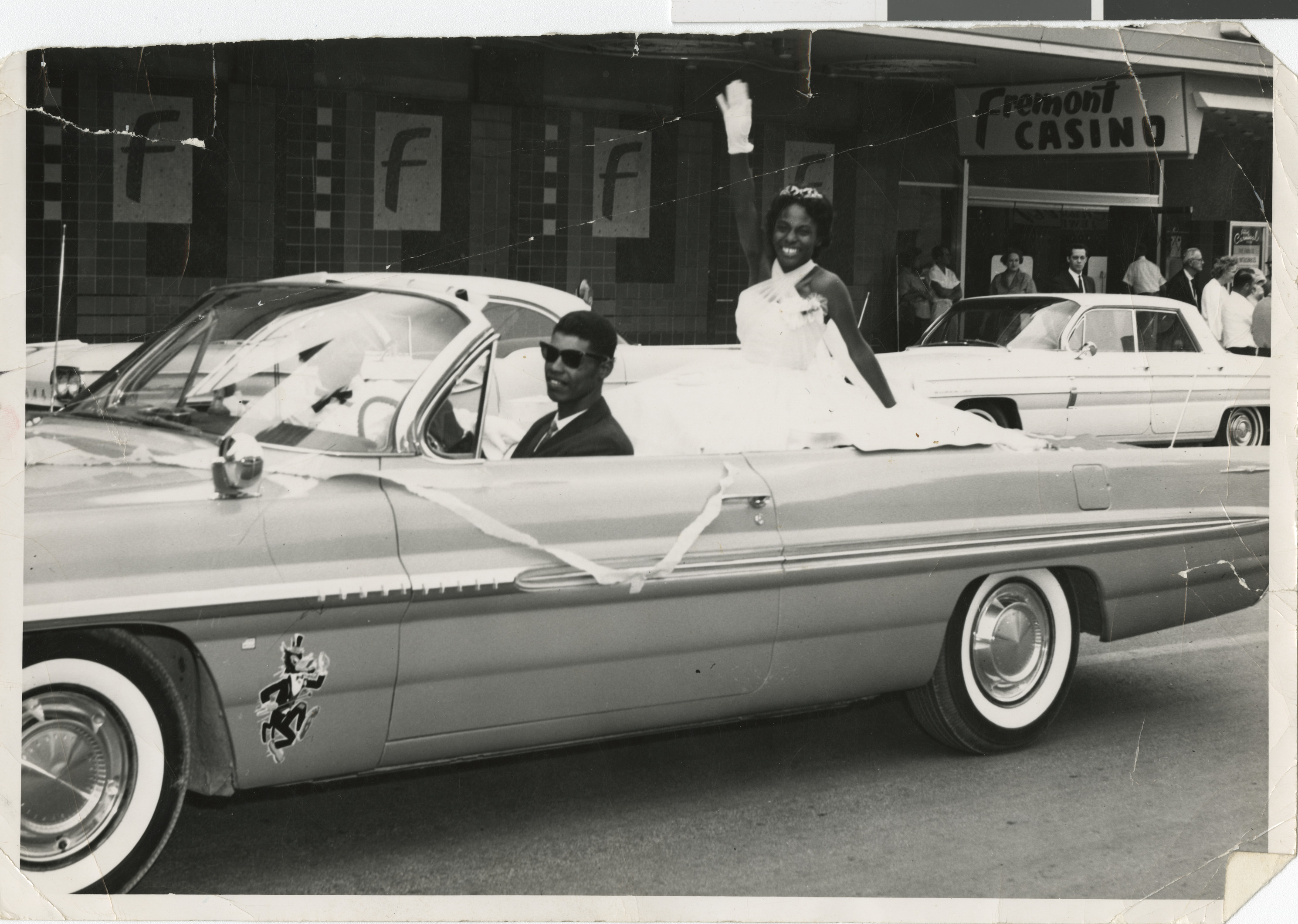 Black and white photograph of Ruby Amie-Pilot riding in the back of a convertible as the International Queen of the Sphinx in front of the Fremont Casino, no date