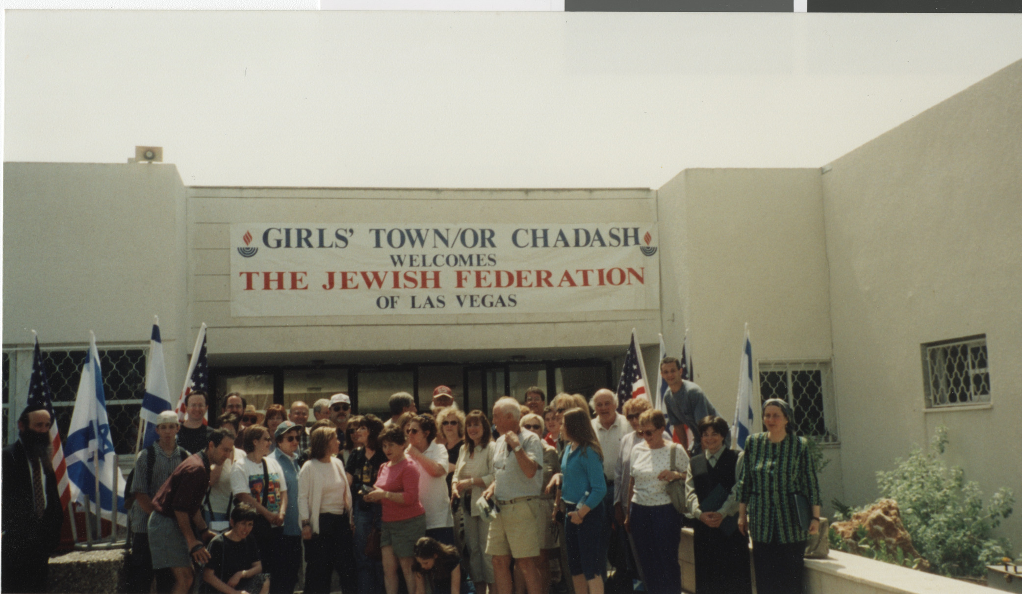 Photograph of group in front of building with sign ""Girls Town/Or Chadash, Welcomes the Jewish Federation of Las Vegas""