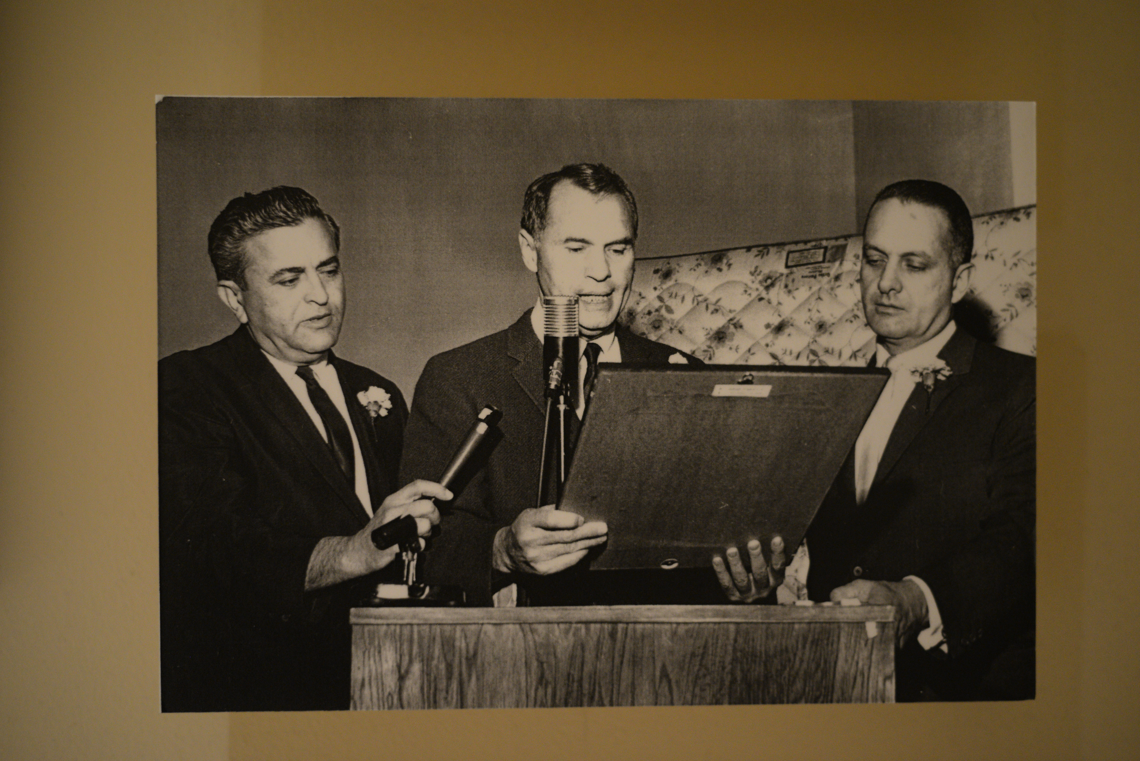 Photograph of Hank Greenspun (center) and others at a podium, date unknown