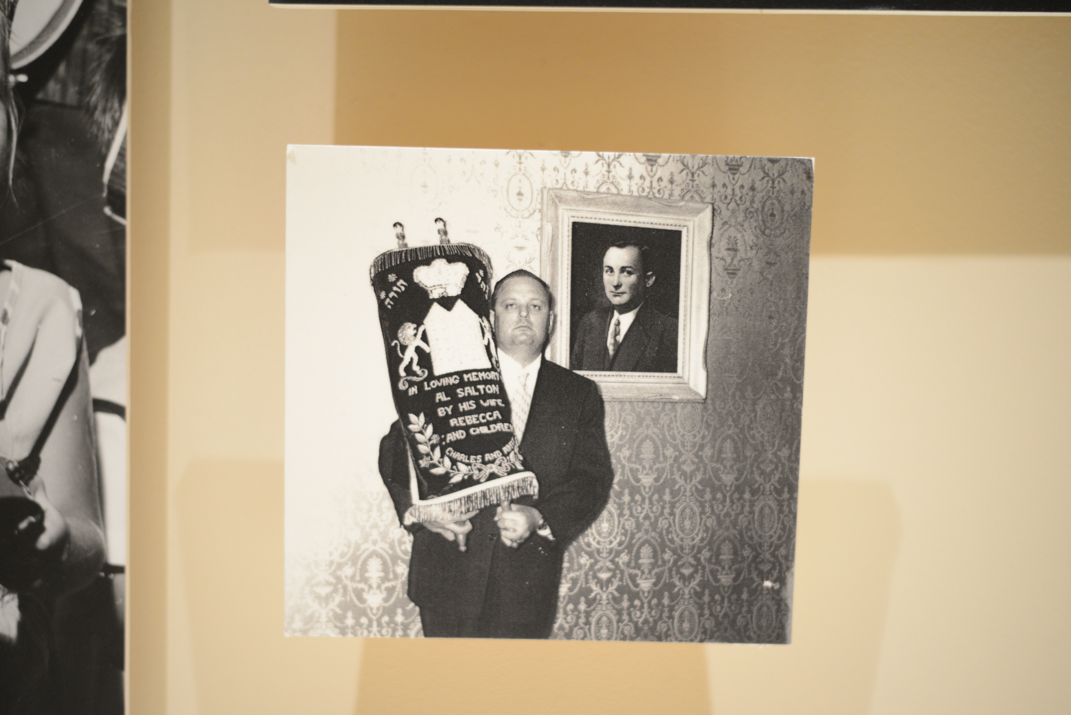 Photograph of man holding Torah scrolls with cover embroidered with ""In loving memory of Al Salton by his wife Rebecca and his children""