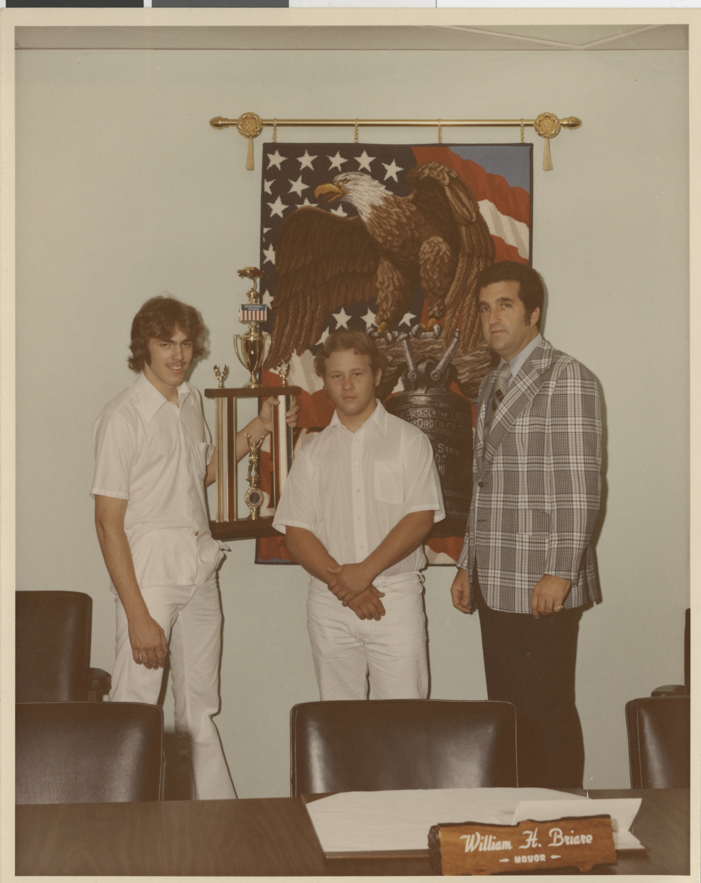 Photograph of Ron Lurie with two young men holding a trophy at the desk of Mayor Bill Briare
