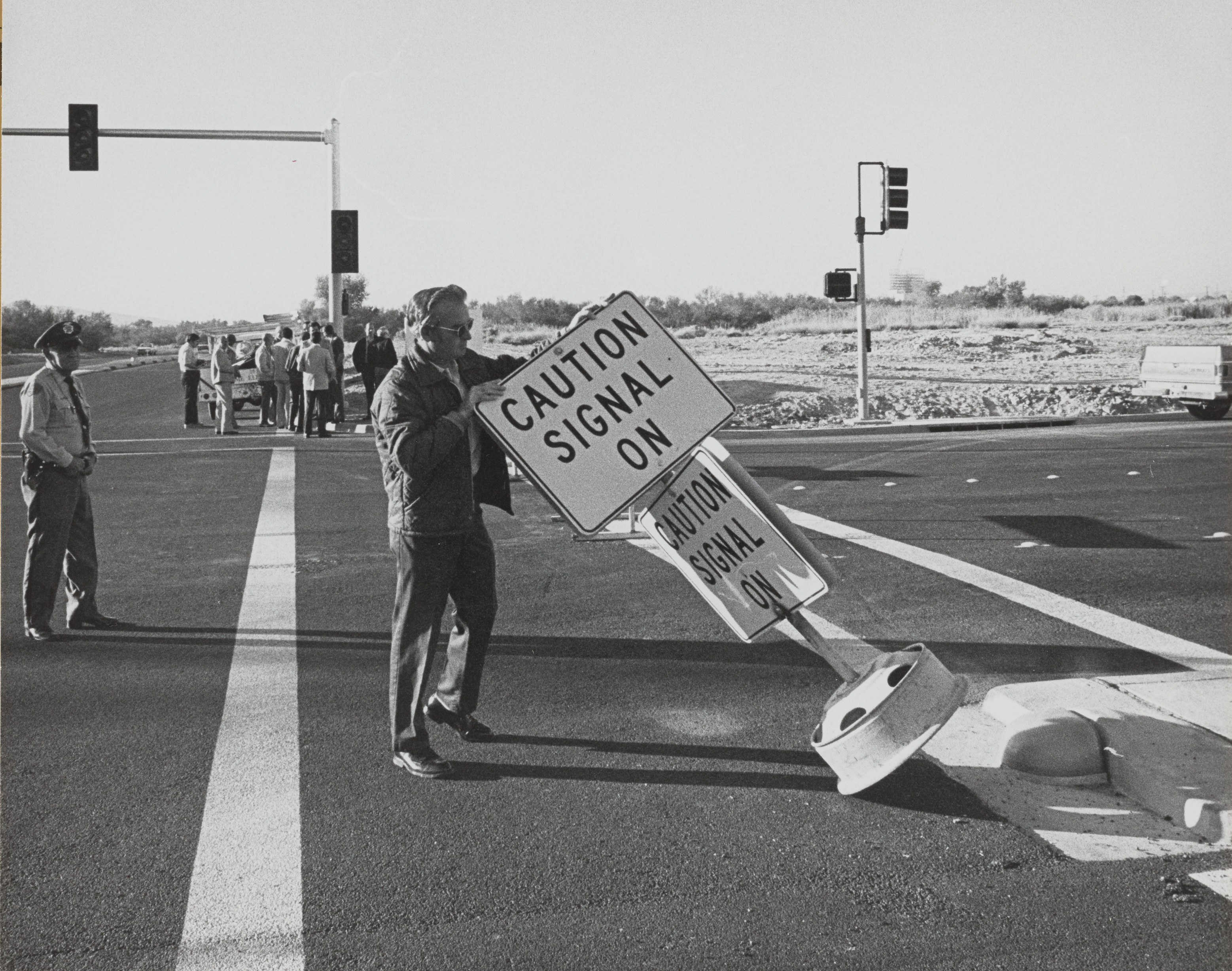 Photograph of man placing sign ""Caution Signal On"" at intersection