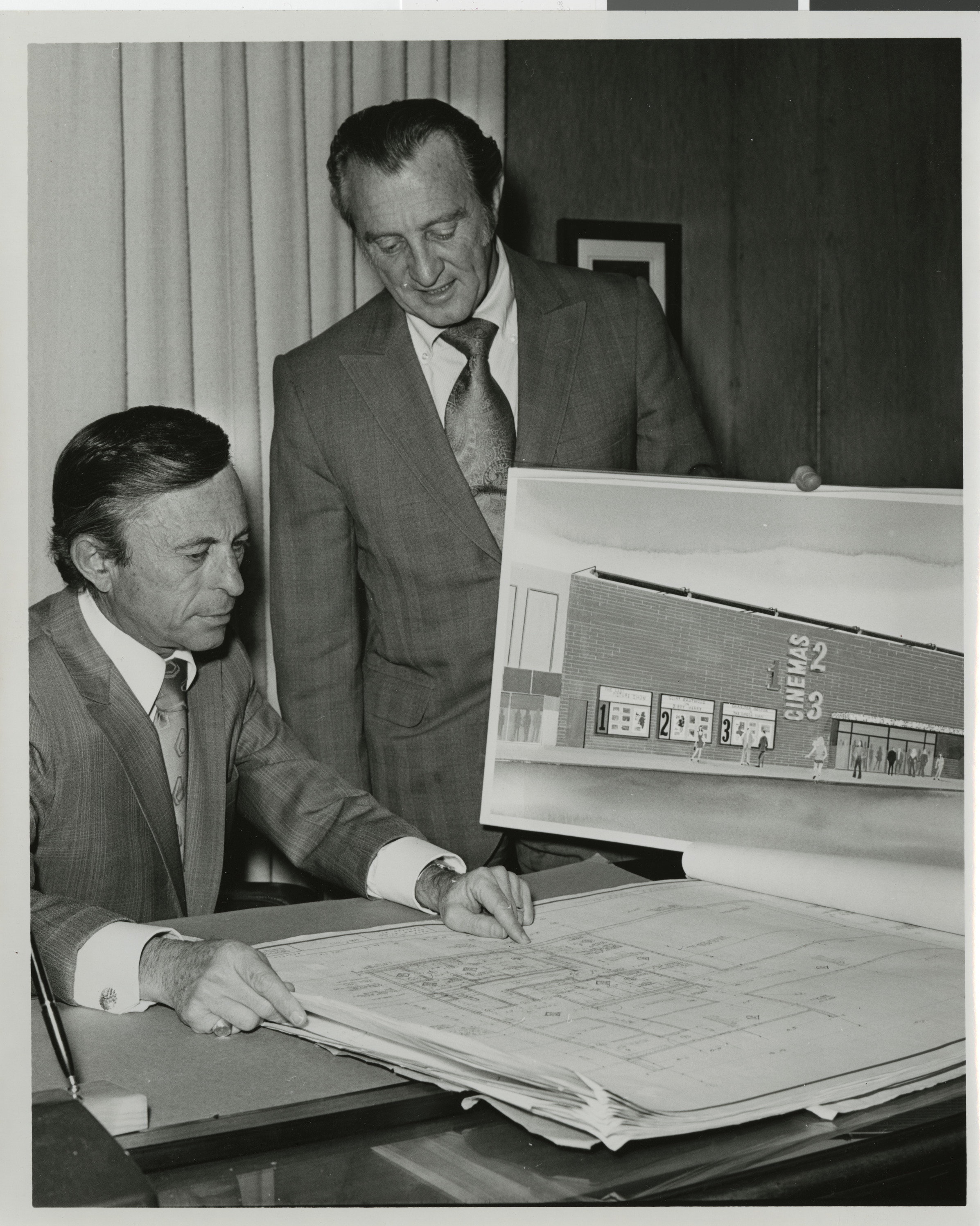Photograph of Lloyd Katz and unknown man with rendering and blue prints for Cinemas 1, 2, 3