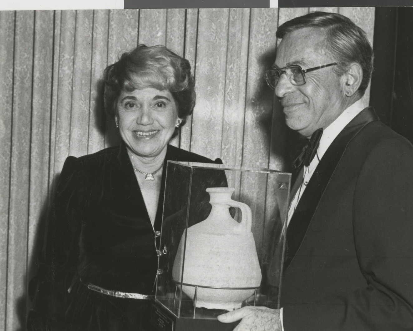 Photograph of Edythe Katz with unknown man holding a terra cotta pot (in a case), which was donated to decorate the Lloyd Katz Honors Lounge at UNLV Library