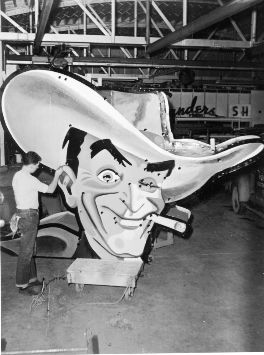 Photograph of worker with Vegas Vic's head in the YESCO shop (Salt Lake City), 1951